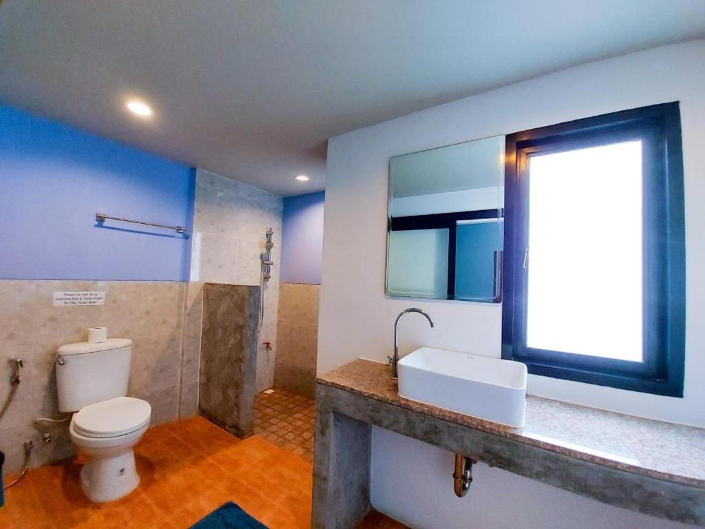 a bathroom with a toilet and a sink and a window at Six Pack Cottage in Chalong 