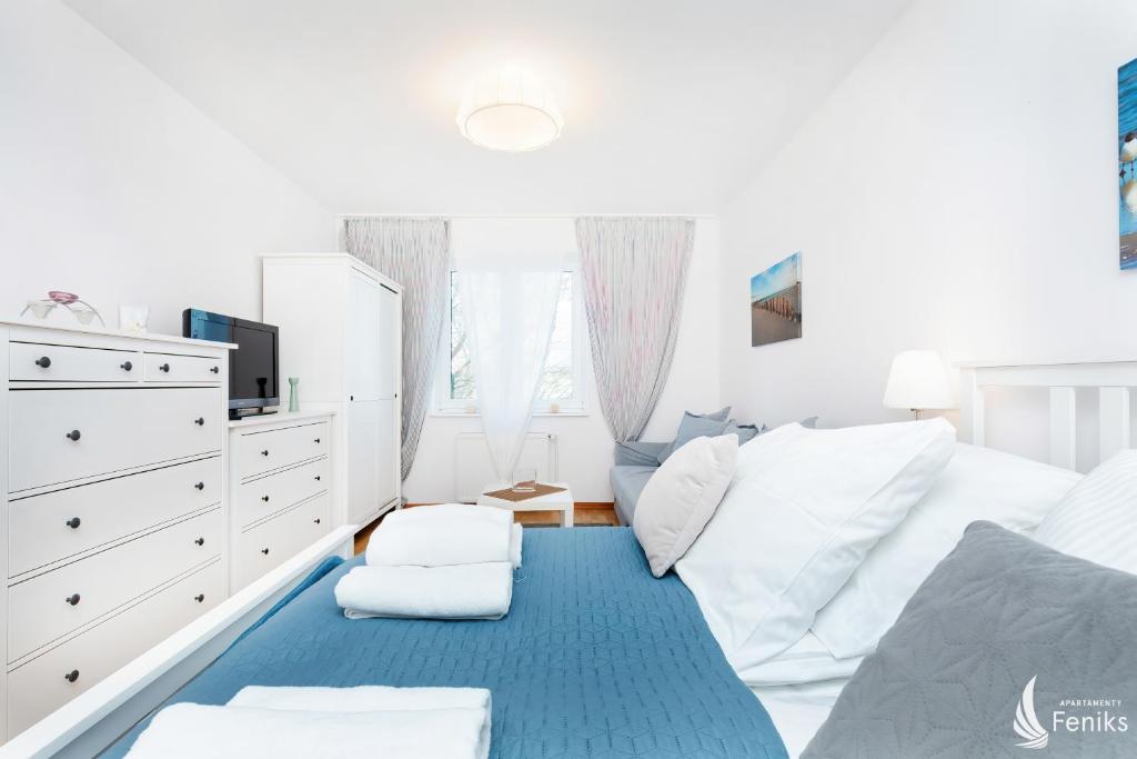 コウォブジェクにあるFeniks Apartamenty - Holiday Homeの白い家具と青い敷物が備わる白いベッドルーム1室