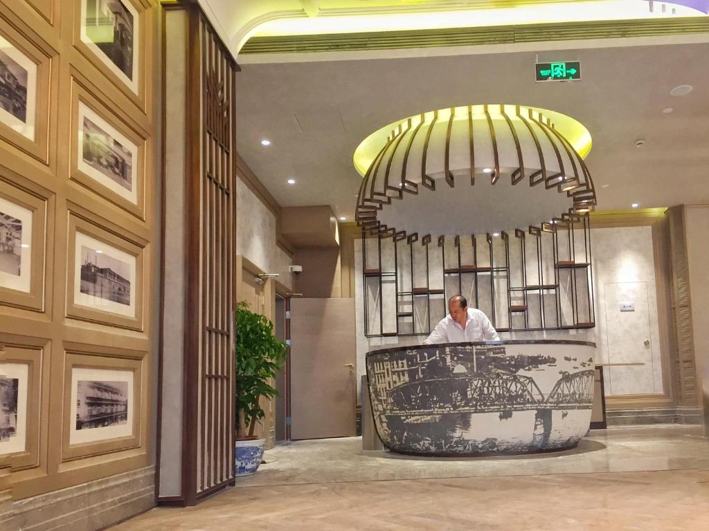 a man standing at a counter in a lobby at Jinjiang Metropolo Hotel Classic Nanjing Road (East) Shanghai in Shanghai