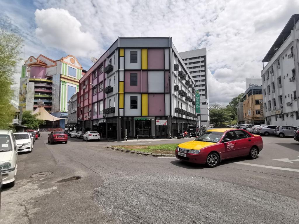 a red car driving down a city street with buildings at D'Green Hotel Kuching in Kuching