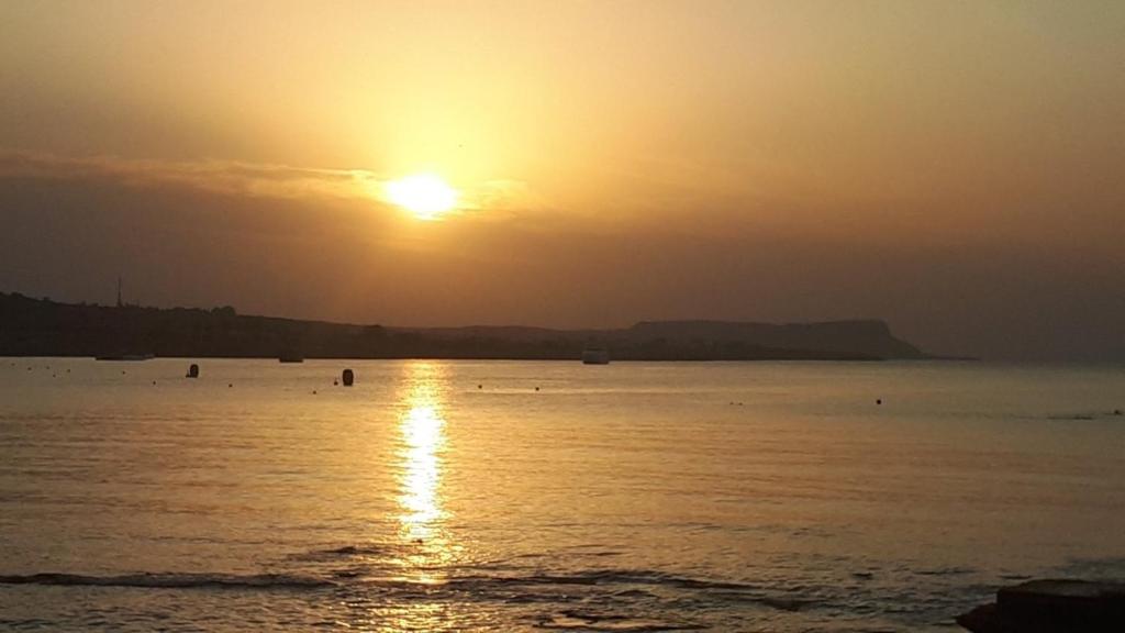 a sunset over the ocean with people in the water at Karousos Beach Rooms in Ayia Napa