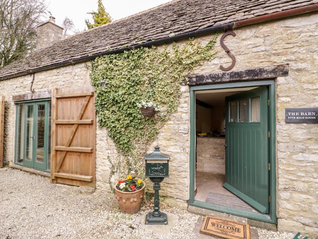 a stone building with a green door and a clock at Five Mile House Barn in Cirencester