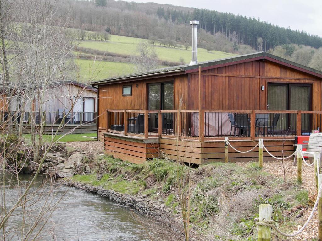 a wooden cabin with a river in front of it at Willow River Lodge in Craven Arms