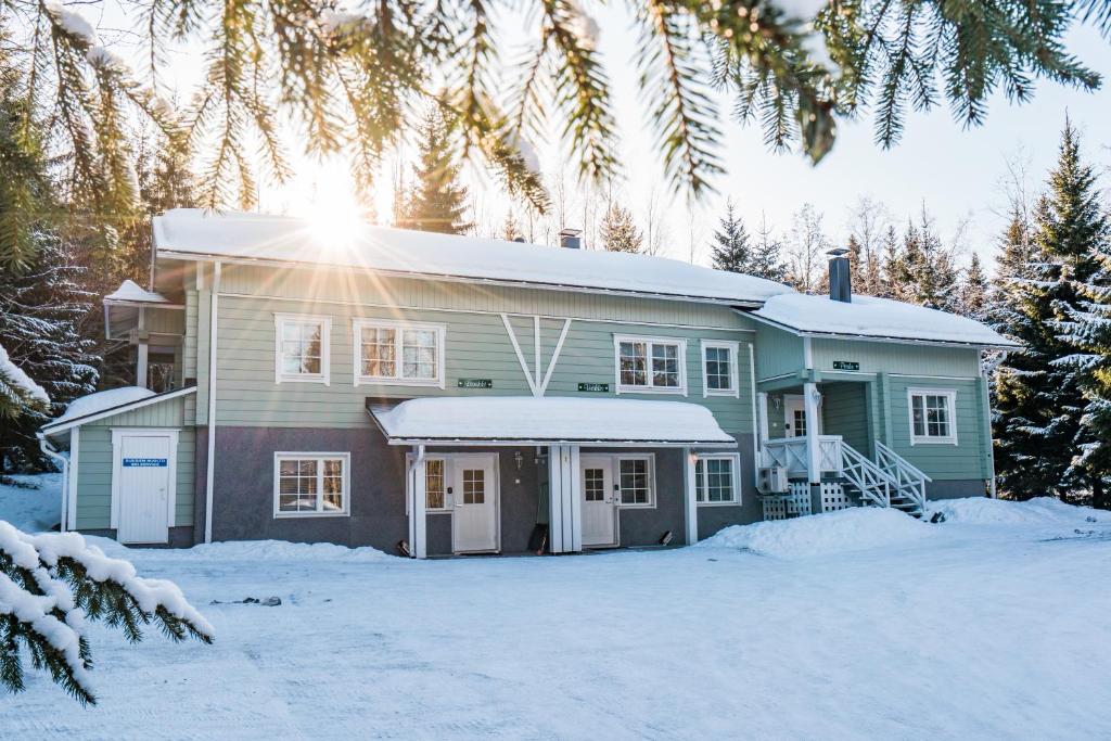 una casa en la nieve con el sol brillando en Lomaperkkiö Apartments, en Vuokatti