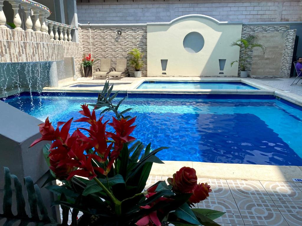 a pool with blue water and red flowers next to it at Hotel Puerta de Oro in Barranquilla