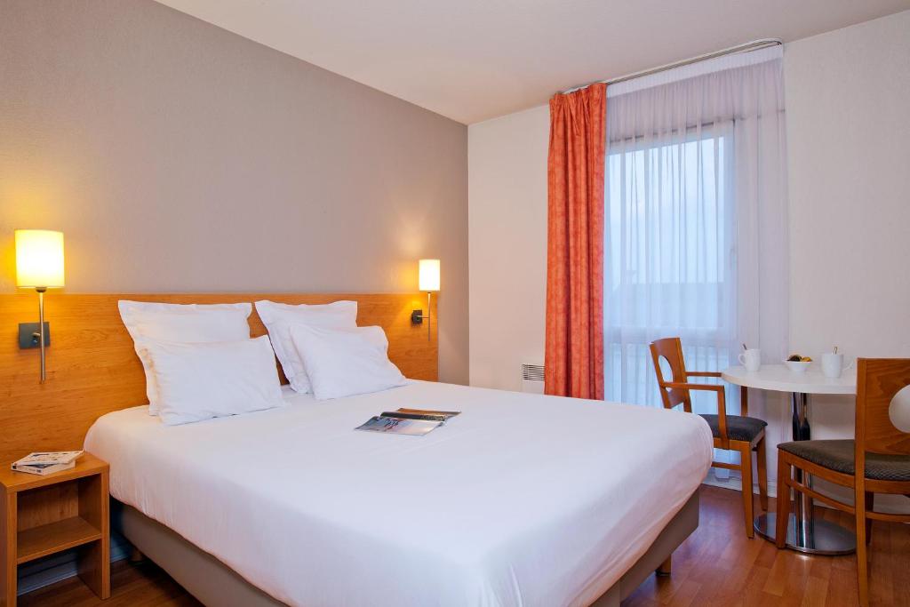 a hotel room with a large white bed and a table at Séjours & Affaires Nantes La Beaujoire in Nantes
