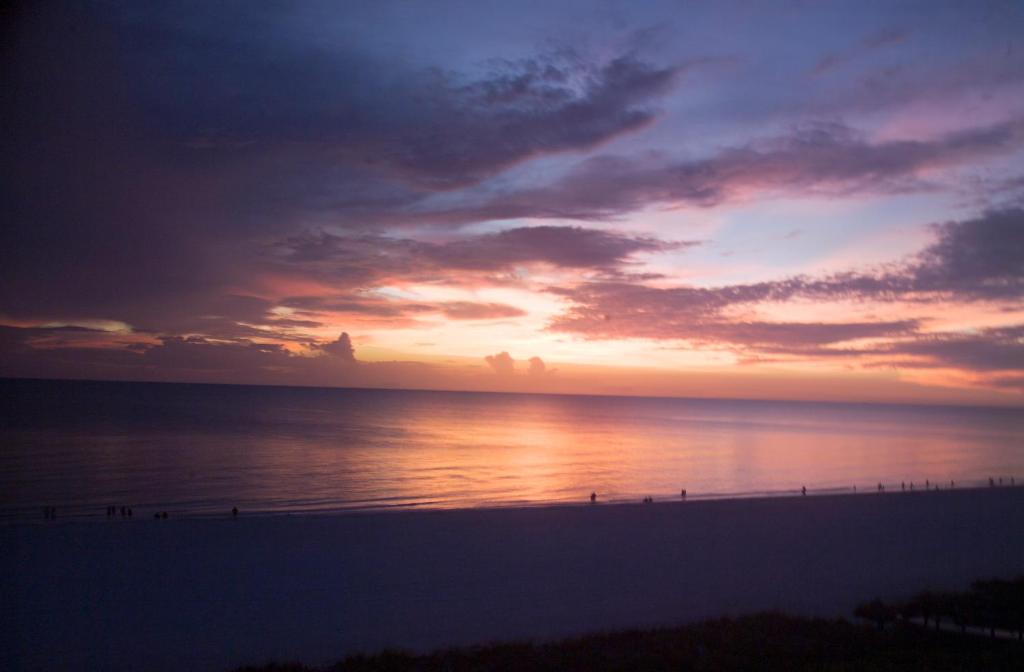 a sunset at the beach with people walking on the beach at Gorgeous views that stretch forever right from your very own private balcony! in Marco Island