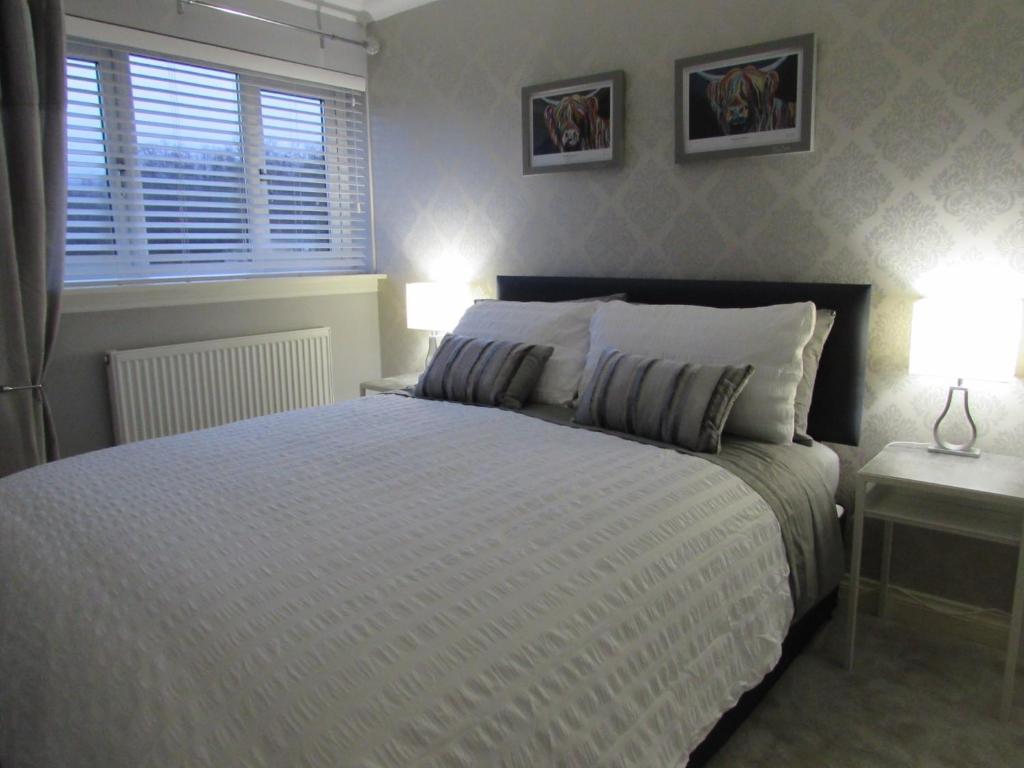 a bedroom with a bed with two lamps and a window at Levenview Holiday Apartment Loch Lom in Balloch