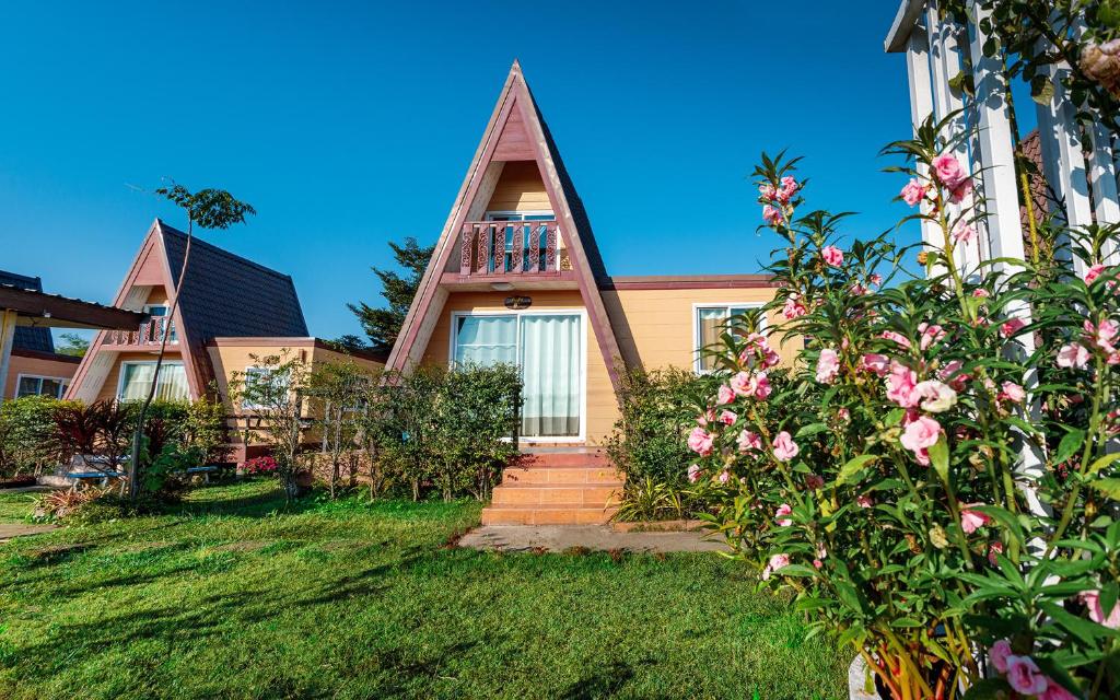 a house with a steep roof and flowers in the yard at Baan Sin Suk in Chiang Rai