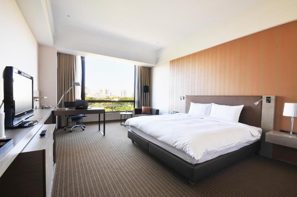 um quarto de hotel com uma cama, uma secretária e uma televisão em Academy Hotel em Tainan