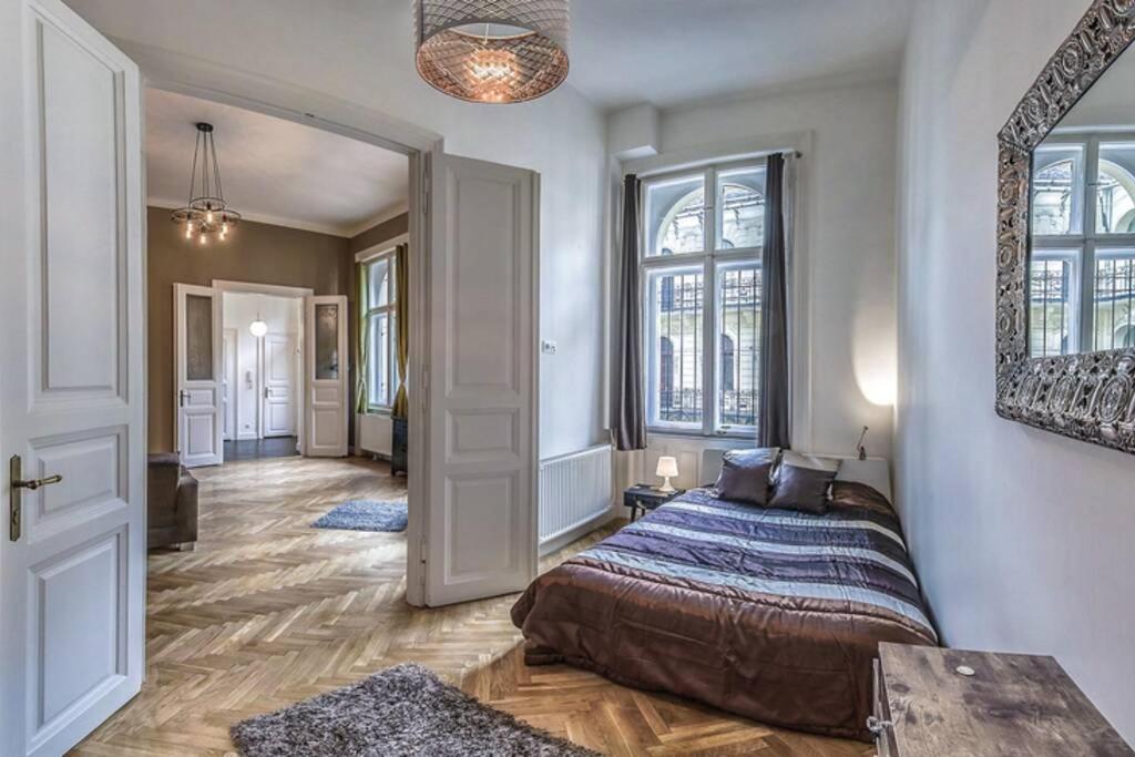 a bedroom with a bed and a hallway with windows at The Suite Mondain Apartment in Budapest