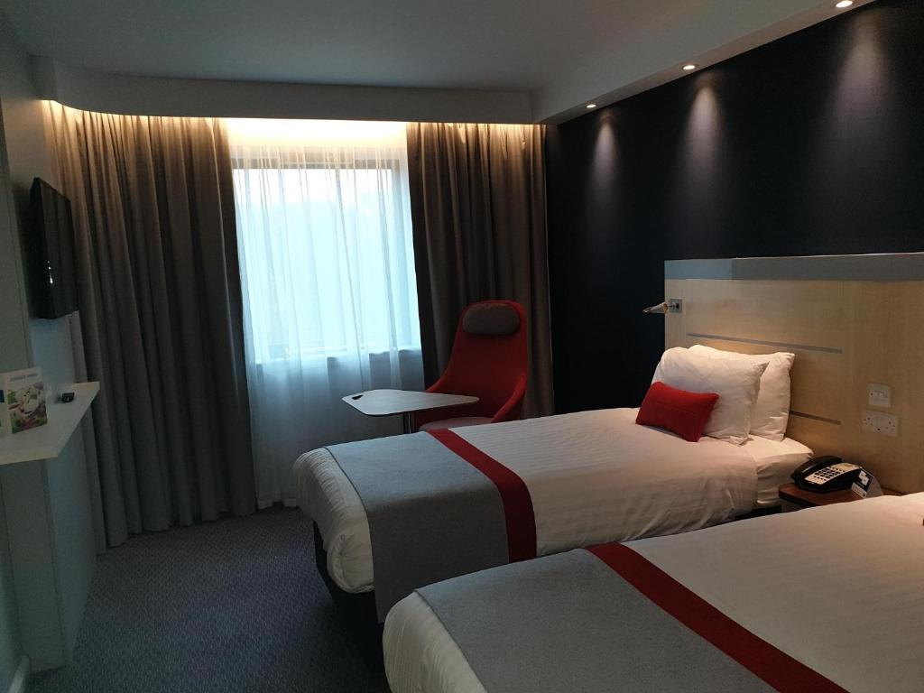a hotel room with two beds and a red chair at Holiday Inn Express Ramsgate – Minster by IHG in Minster