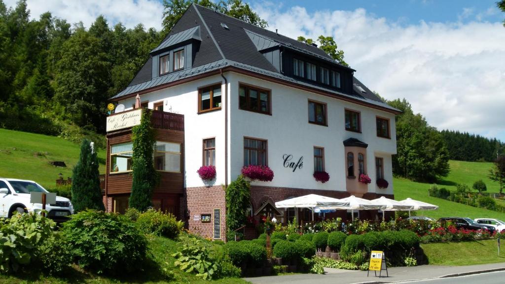 een groot wit gebouw met een zwart dak bij Café & Gästehaus Reichel in Bärenstein