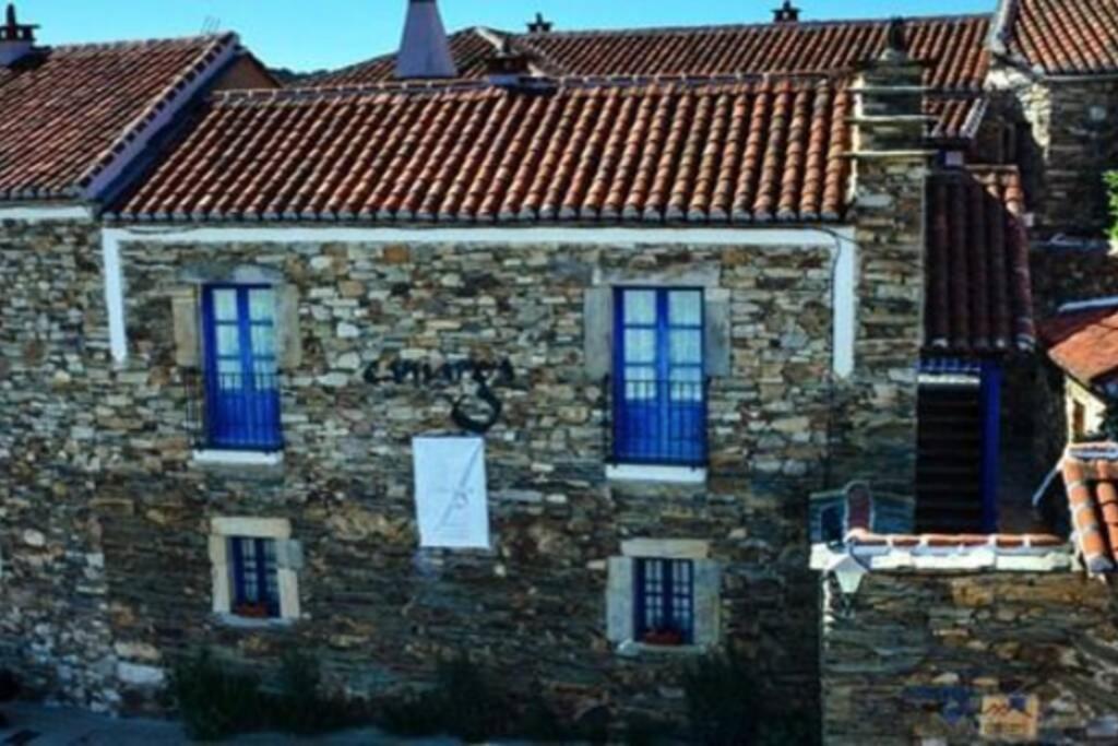 Casa de piedra con ventanas azules y techos rojos en CASA CAMARGA en Santiago Millas
