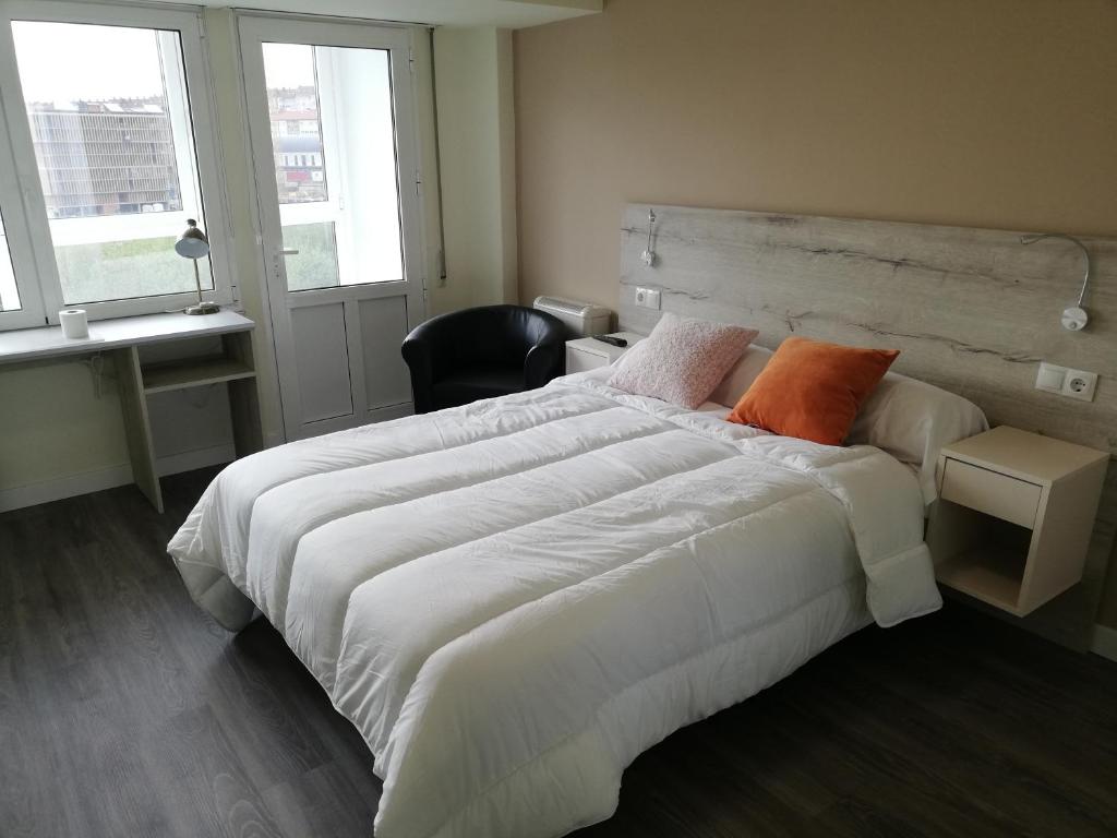 a bedroom with a large bed with white sheets and orange pillows at Pensión La Intermodal in Santiago de Compostela