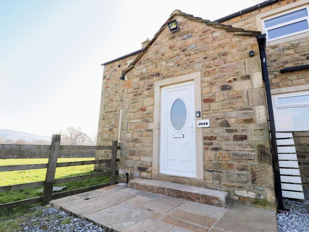 a brick building with a white door and a fence at Jess Cottage in Skipton