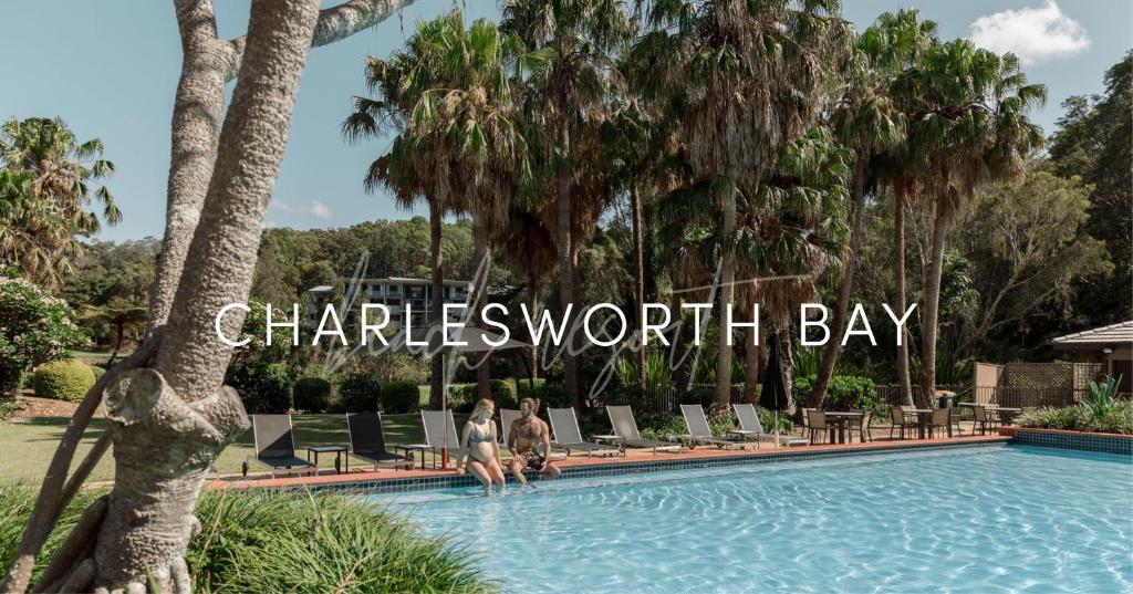 twee mensen staan in een zwembad met een bord dat Charliesworth Bay leest bij Charlesworth Bay Beach Resort in Coffs Harbour