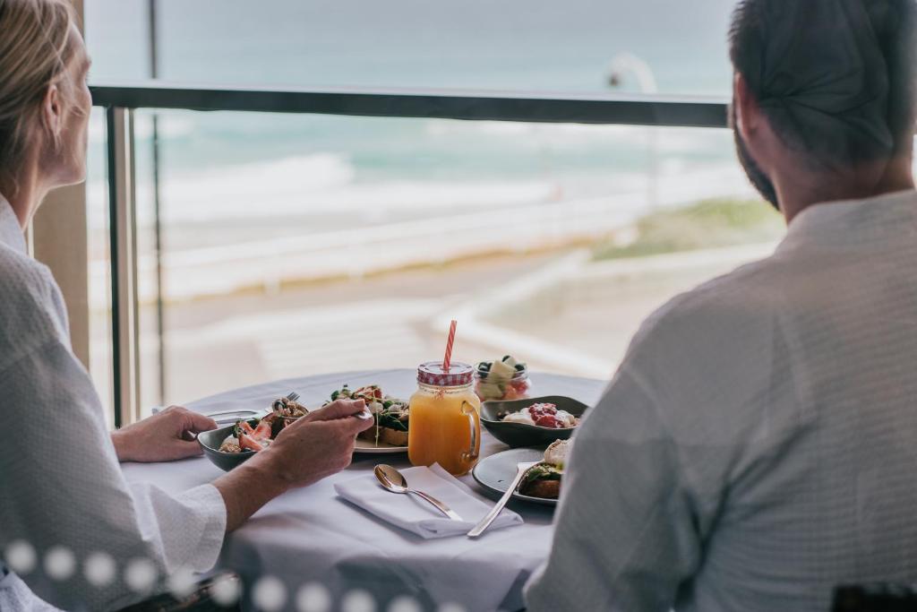 two people sitting at a table with a plate of food at Novotel Newcastle Beach in Newcastle