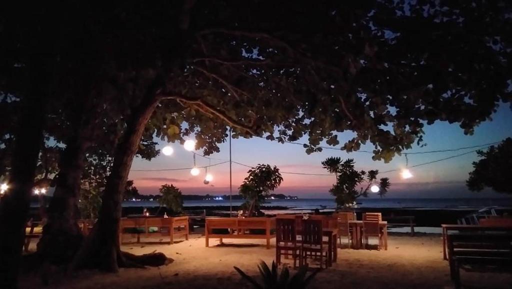 un groupe de tables et de chaises sous un arbre la nuit dans l'établissement Salili Bungalow, à Gili Air