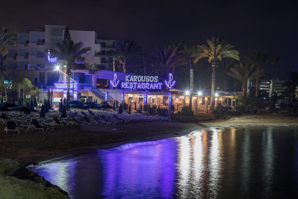 a building with a sign on the beach at night at Karousos Beach Rooms in Ayia Napa