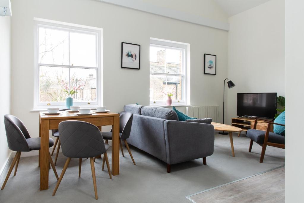 uma sala de estar com um sofá, uma mesa e cadeiras em Queens Park by Viridian Apartments em Londres