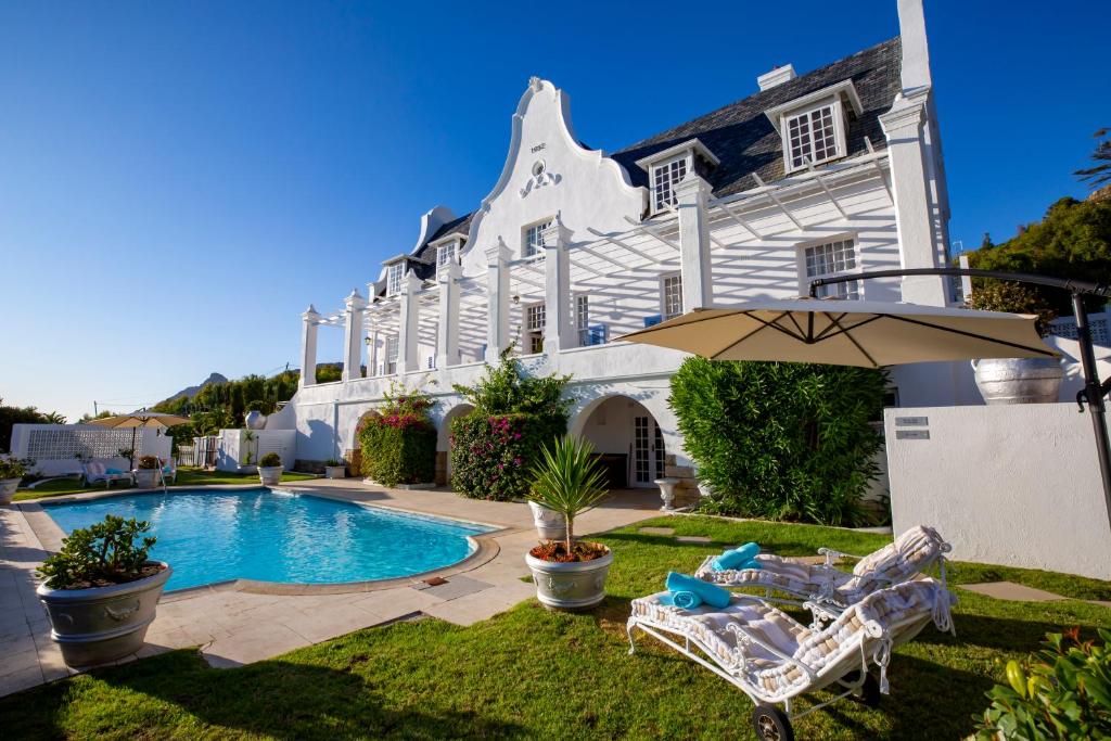 a house with a swimming pool and two chairs and an umbrella at Stillness Manor Estate & Spa in Constantia