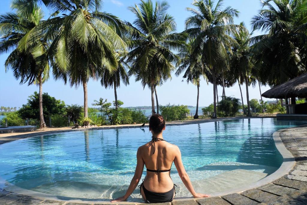 a woman in a bikini sitting next to a swimming pool with palm trees at Kitelantis Hotel and Resort in Kalpitiya
