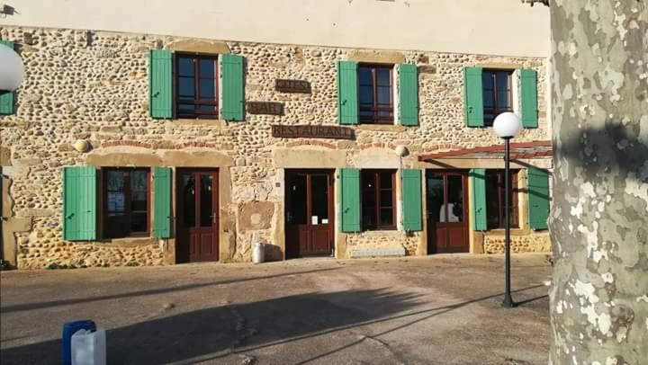 un bâtiment en pierre avec des fenêtres vertes à volets et une lumière de rue dans l'établissement Gîte - Auberge du Midi, à Saint-Antoine