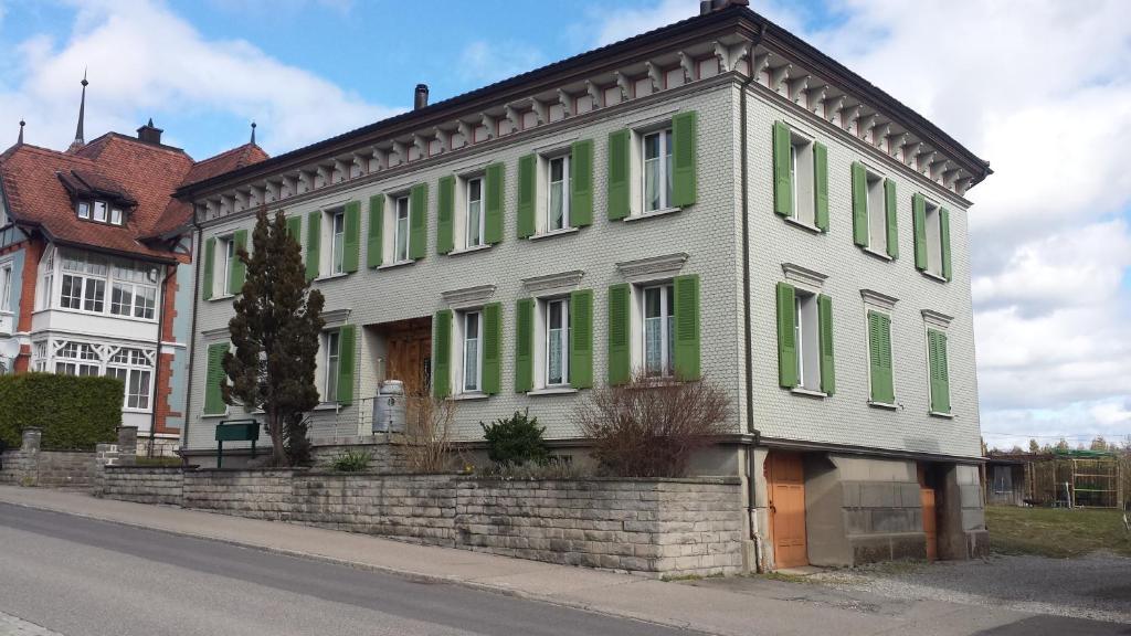 ein älteres Haus mit grünen Rollläden auf einer Straße in der Unterkunft Tor zum Toggenburg in Bazenheid