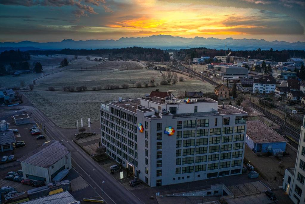 ein hohes weißes Gebäude mit Sonnenuntergang im Hintergrund in der Unterkunft Hotel Swiss Star in Wetzikon