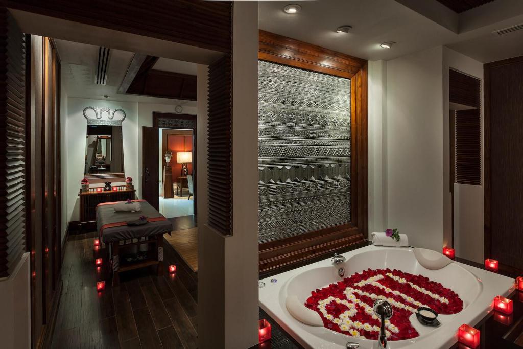 A bathroom with a petal-filled soaking tub, candles, and a treatment table beyond.