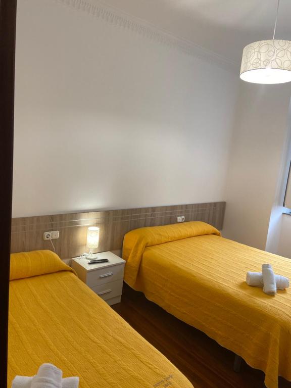 two beds in a room with yellow sheets at Pensión Hedrass in Santiago de Compostela