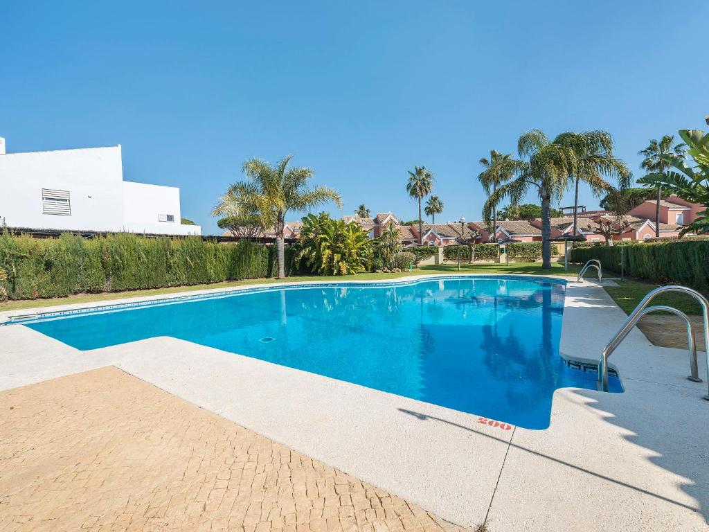 a large blue swimming pool with palm trees and houses at Holiday Home Brisamar - Novo Sancti Petri by Interhome in Chiclana de la Frontera