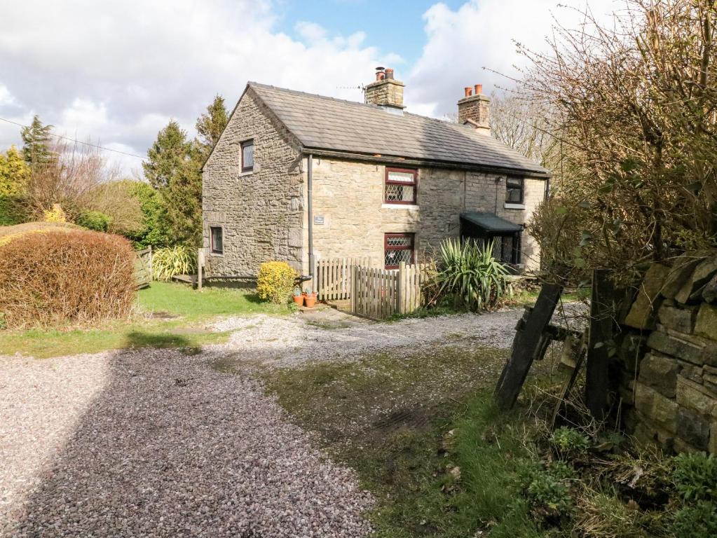 una vieja casa de piedra con una valla delante de ella en The Cottage Glossop, en Glossop