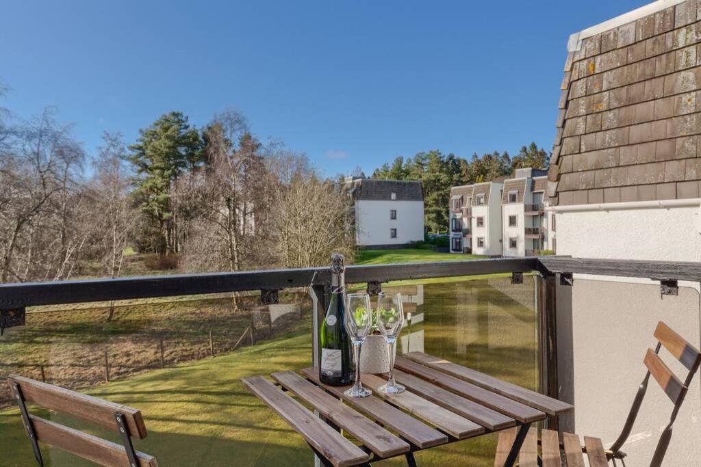 un tavolo in legno con bottiglie di vino e bicchieri sul balcone di 45 Guthrie Court, Fantastic top floor apartment next to Gleneagles ad Auchterarder