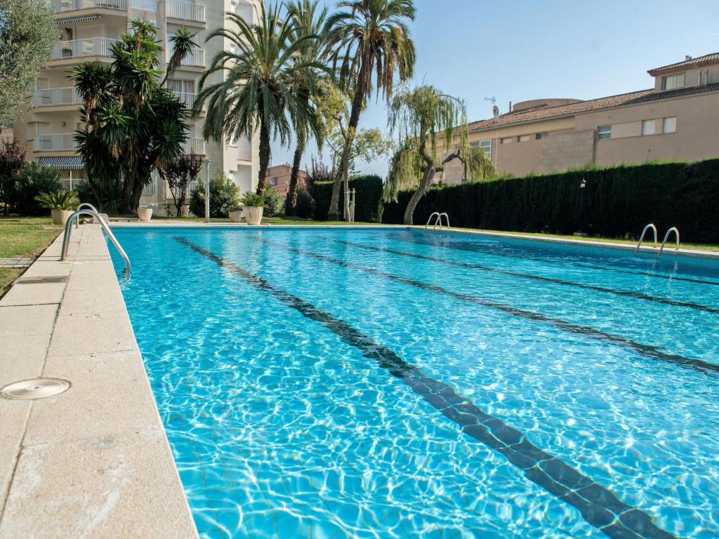 a blue swimming pool with palm trees and a building at Apartment Edificio Blanqueries-2 by Interhome in Calella