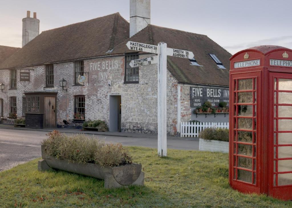 uma cabine telefónica vermelha e um sinal de rua em frente a um edifício em The Five Bells Inn em Brabourne