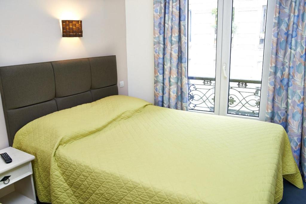 a bedroom with a yellow bed and a window at Hotel Luxor in Issy-les-Moulineaux