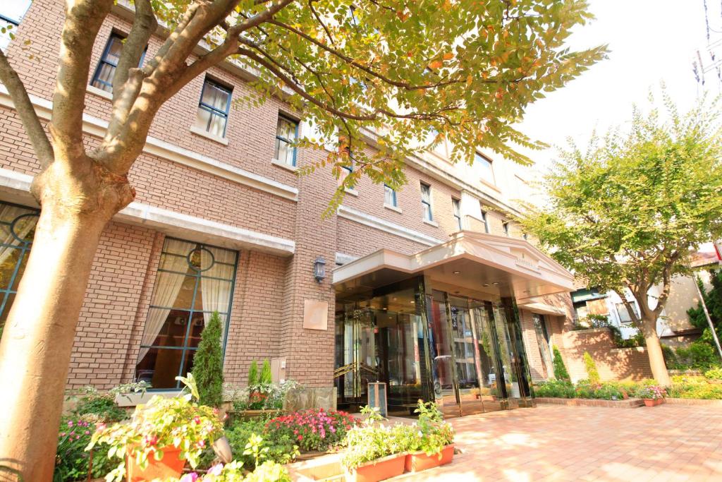 un edificio de ladrillo con un árbol delante de él en Quintessa Hotel Sasebo en Sasebo