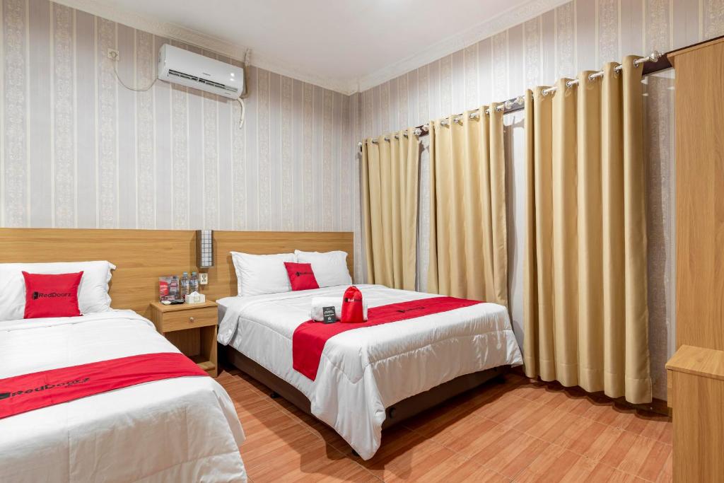 una camera d'albergo con due letti con accenti rossi di RedDoorz Syariah @ Danau Kerinci Sawojajar a Ngadipuro