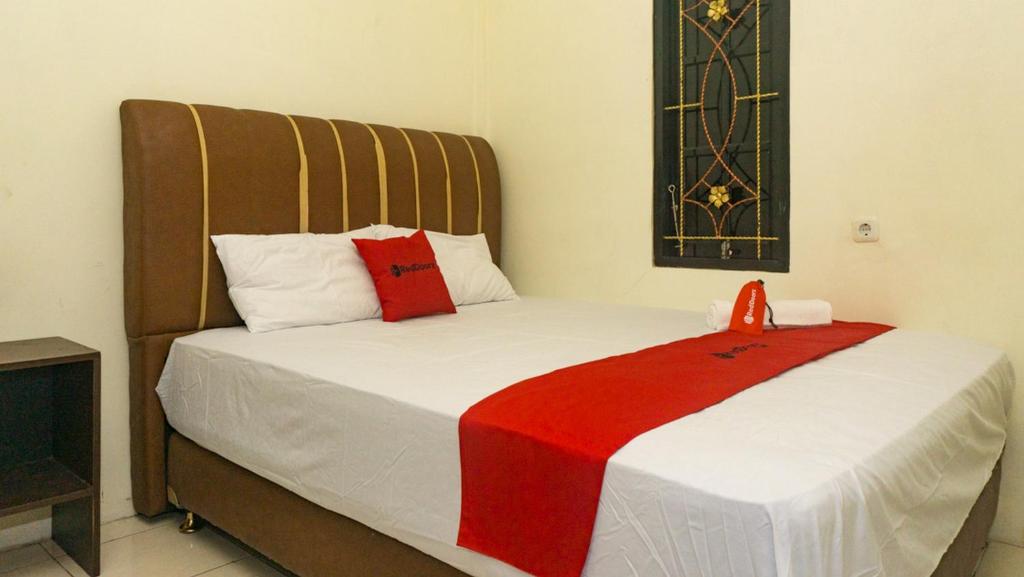 a bedroom with a bed with a red blanket on it at RedDoorz near Sentani Airport Jayapura in Jayapura