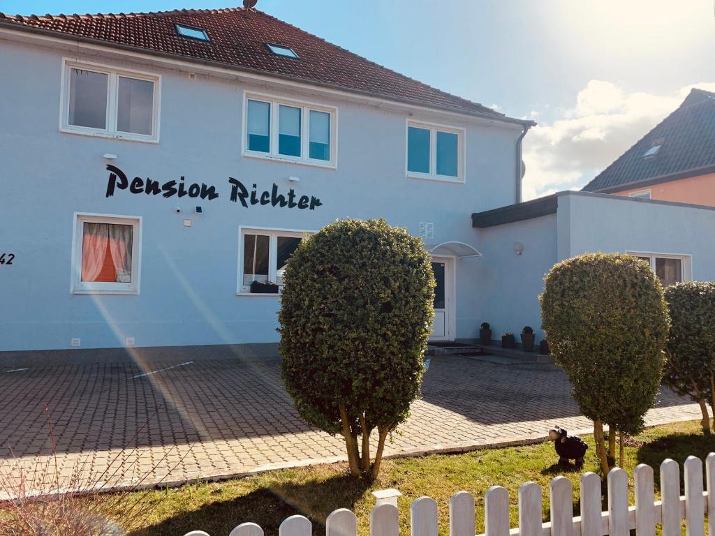 a white building with a white fence and trees at Pension Richter in Ostseebad Nienhagen