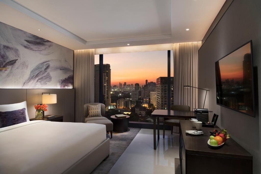 Evening room view with a king bed, work desk and illuminated Bangkok skyline.
