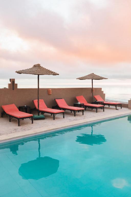a pool with chairs and umbrellas on a building at Le Nid d'Aigle in Mirleft
