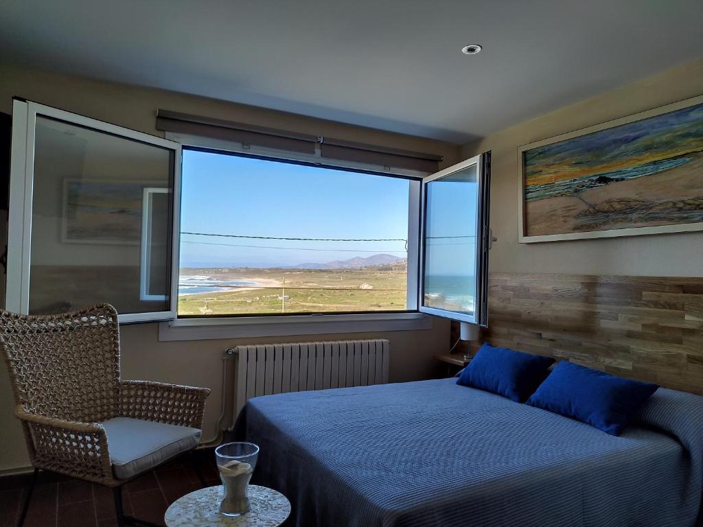 a bedroom with a bed and a chair and a window at Hostal Balieiros Corrubedo in Corrubedo