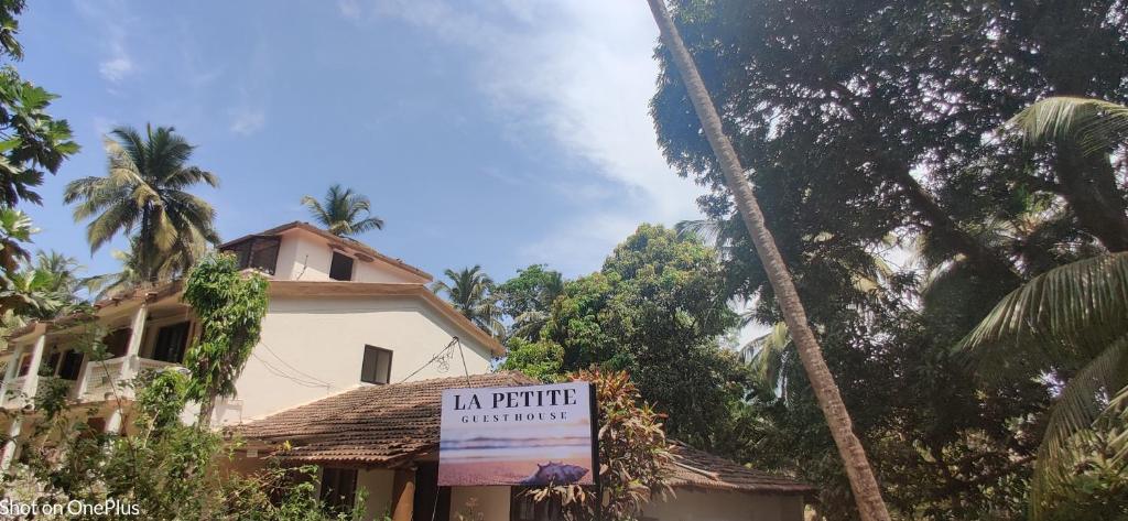a sign in front of a house with a palm tree at La Petite Guest House in Bogmalo