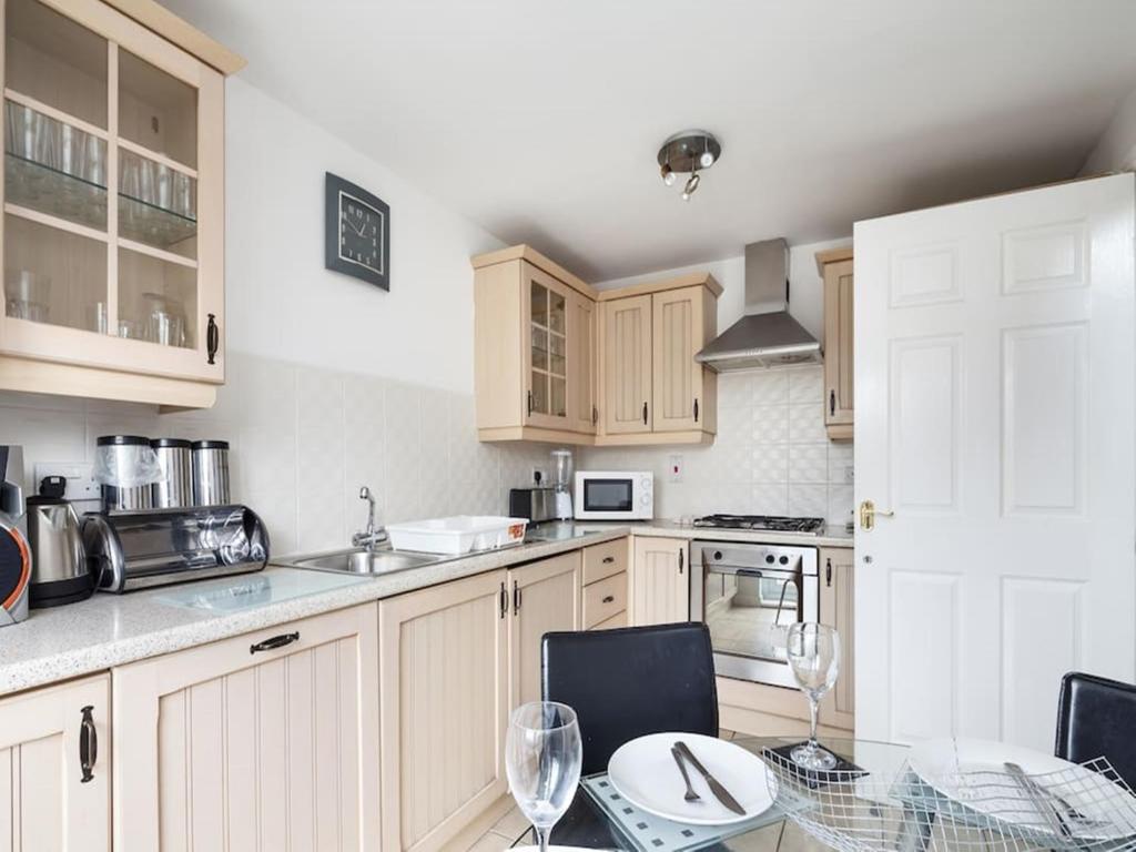 una cocina con armarios de madera y una mesa con sillas. en My-Places Abbotsfield Court Townhouse 4, en Mánchester