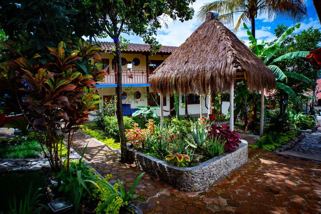 un complejo con un jardín con flores y techo de paja en Hostal Jardín Escondido, en Vilcabamba