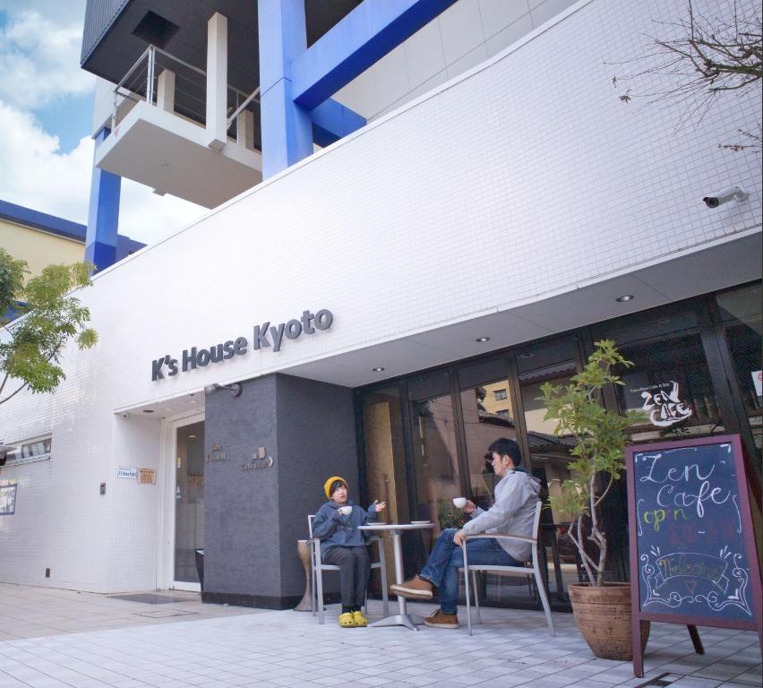 京都的住宿－K's House Kyoto -Travelers Hostel，两个人坐在商店外的椅子上