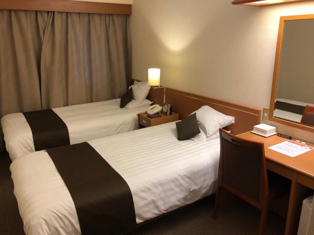 a hotel room with two beds and a desk at Daiichi Inn Ikebukuro in Tokyo
